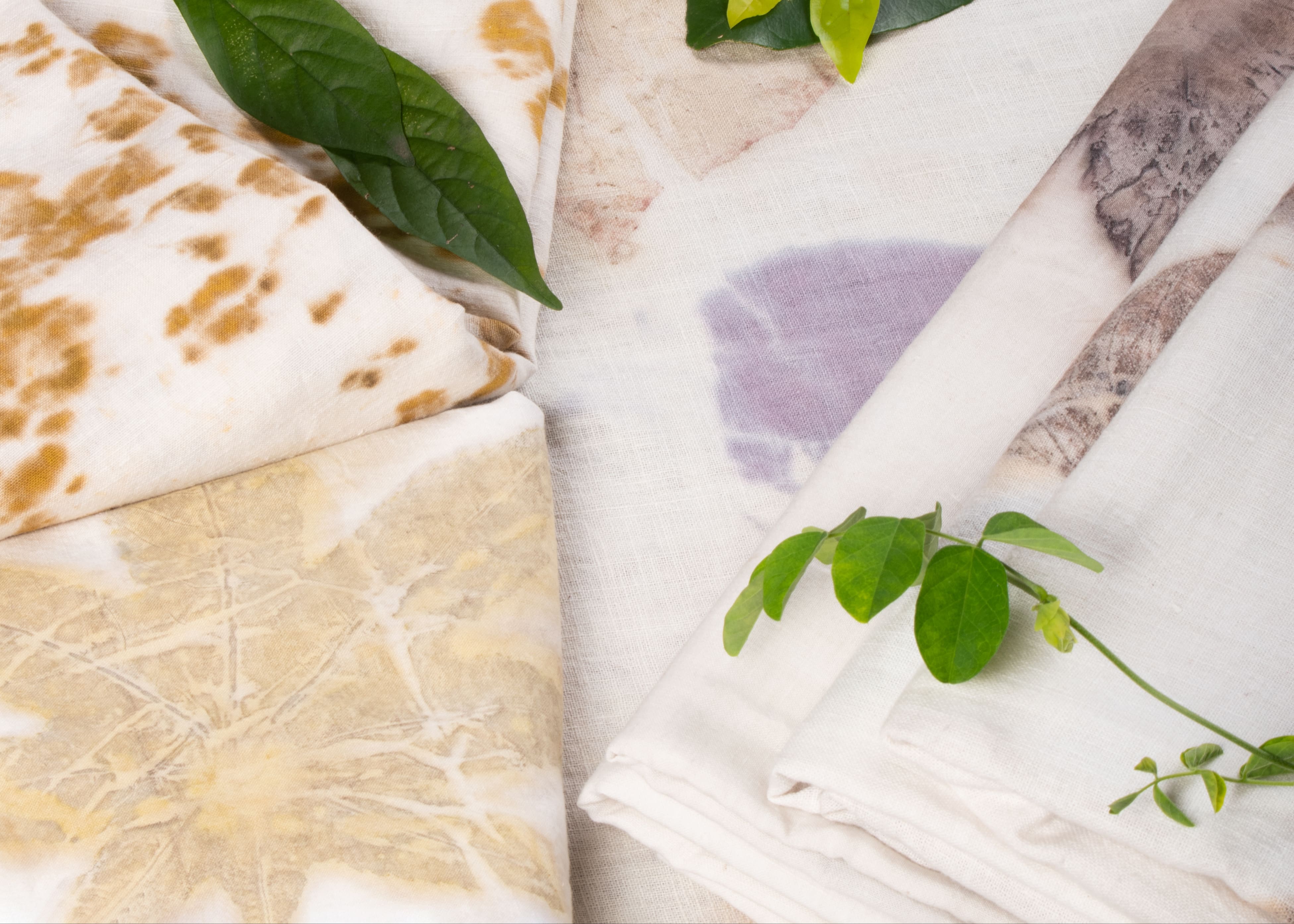 Leaf printed eco print fabric collection featuring handcrafted botanical impressions on natural textiles with fresh green leaves arranged in a flat-lay composition.